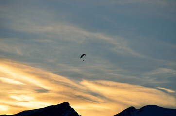 Fototapeta na wymiar Paraglider on vibrant colourful dawn sky with majestic snow covered mountain underneath in the arctic circle