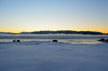 dense ice fog in winter over fjord and mountain landscape at colorful sunset