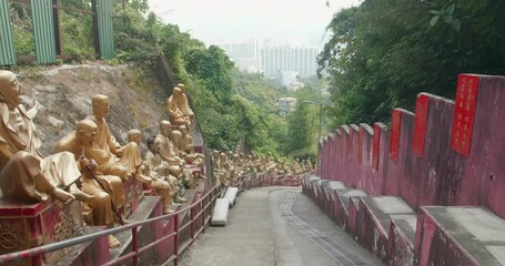 Tracking out (TUT) of buddha statues in rows. Ten Thousand Buddhas Monastery's main alley stairs, Sha Tin, Hong Kong. Peaceful golden religious sculptures. High dynamic range footage.