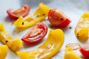 Slices of yellow bell pepper and red tomato prepared for baking with spices, close up