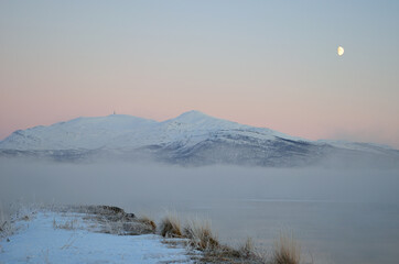 pink sunset sky in winter over frozen fjord and dense ice fog