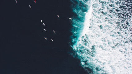 Top view from drone of a group of surfers seek to the ocean to catch next beautiful wave during surf lessons in Bali school. Just came down wave and people floating on surf boards. Background for blog © BullRun