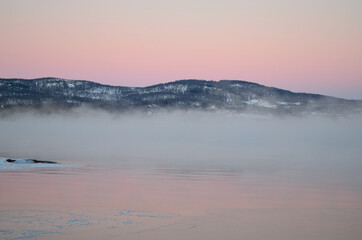 pink sunset sky in winter over frozen fjord and dense ice fog