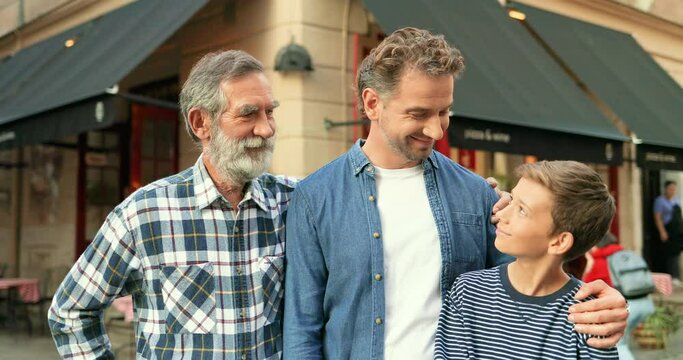 Portrait of happy Caucasian male family generations at cafe on street posing to camera. Cute teen boy with handsome father and grandfather. Senior man with son and grandson smiling and embracing.