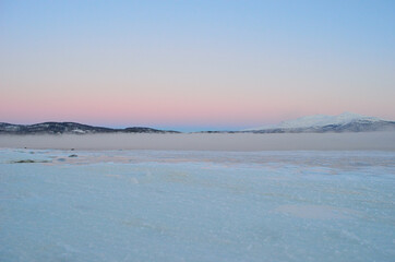 pink sunset sky in winter over frozen fjord and dense ice fog