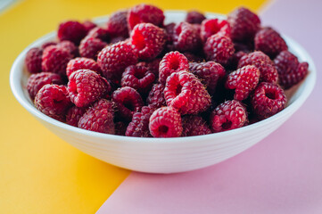 a beautiful light blue bowl of fruit with raspberries, blueberries and blackberries on yellow background, top view, studio shot