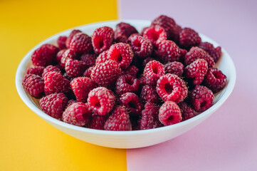 a beautiful light blue bowl of fruit with raspberries, blueberries and blackberries on yellow background, top view, studio shot