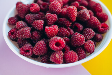 a beautiful light blue bowl of fruit with raspberries, blueberries and blackberries on yellow background, top view, studio shot