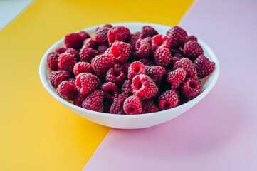 a beautiful light blue bowl of fruit with raspberries, blueberries and blackberries on yellow background, top view, studio shot