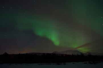 magnificent aurora borealis over frozen river bed and snowy mountain in the cold arctic circle night