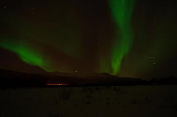 incredible strong aurora borealis over snowy mountain and frozen river bed in winter landscape