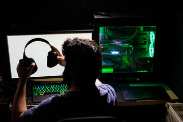 gamer wearing headphones on preparing for e-sport in front of green rgb computer