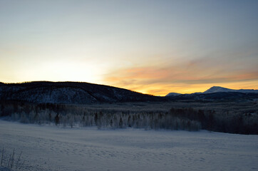 Scenic snowy mountain with vibrant colourful sky and white frost covered forest in the front