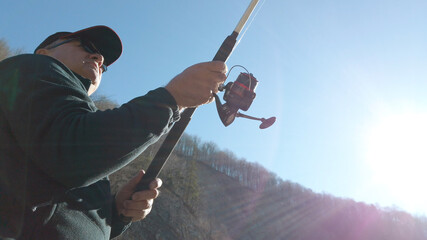 Adult man fishing at mountain stream. Throws a fishing rod into the river at the rocky terrain....