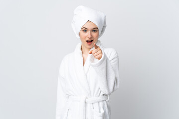 Teenager girl in a bathrobe isolated on white background surprised and pointing front