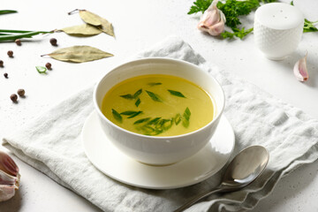 Chicken broth with spices, greens, garlec, parsley, onion in white bowl on white table. Copy space. Close up.