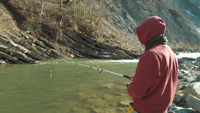 Adult man fishing at mountain stream. Throws a fishing rod into the river at the rocky terrain. Rolling the reel with fishing line.