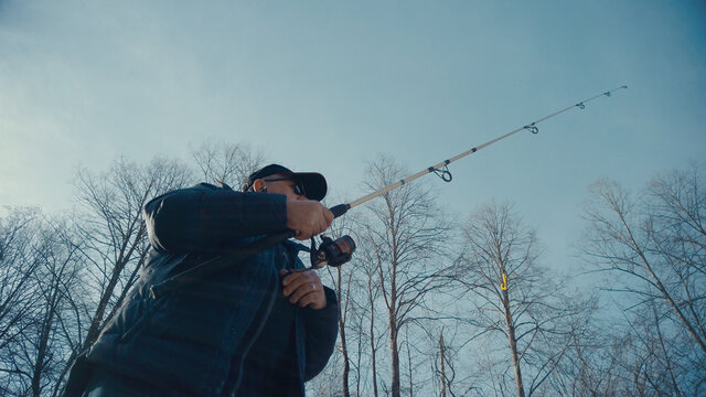 Adult man fishing at mountain stream. Throws a fishing rod into the river at the rocky terrain. Rolling the reel with fishing line.