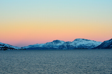 Vibrant colours on dawn sky over cold arctic fjord water and majestic snowy mountain range