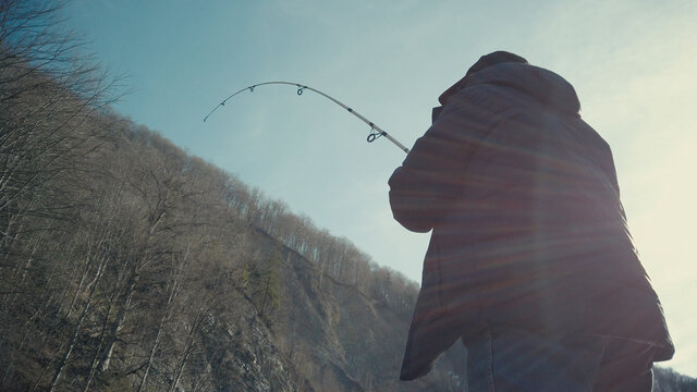 Adult man fishing at mountain stream. Throws a fishing rod into the river at the rocky terrain. Rolling the reel with fishing line.