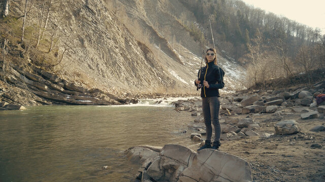 Fisherwoman fishing at mountain stream. Throws a fishing rod into the river at the rocky terrain. Rolling the reel with fishing line. Female fisher. Gender equality