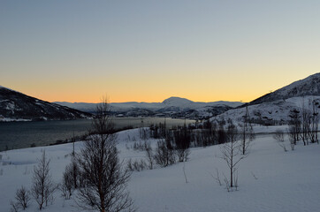 Fototapeta na wymiar Beautiful snowy winter landscape with vibrant colourful dawn sky, majestic mountains and cold fjord water