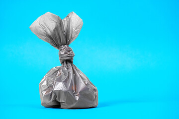 Close up plastic bag gathering with dog poop droppings on a blue background. Eco friendly solution for pet owners