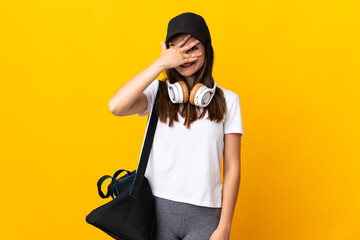 Young sport woman with sport bag isolated on yellow background covering eyes by hands and smiling