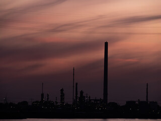 Silhouette of industrial enterprise chimneys in the city on the river bank on a sunset.