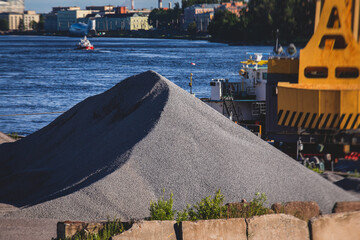 Bulk-handling crane unloading sand, road metal and gravel from cargo vessel ship, heavy vehicle and...