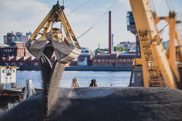 Bulk-handling crane unloading sand, road metal and gravel from cargo vessel ship, heavy vehicle and...