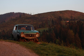 Vintage devastated car abandoned on a mountain peak by sunset