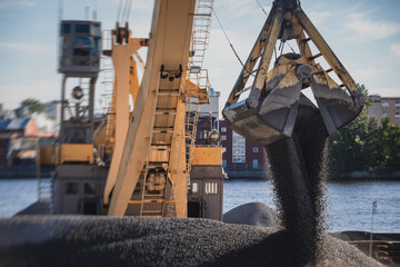 Bulk-handling crane unloading sand, road metal and gravel from cargo vessel ship, heavy vehicle and...