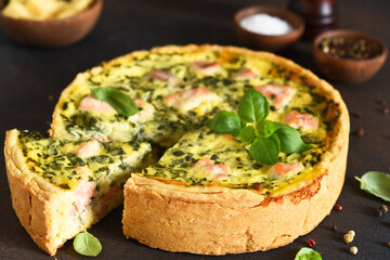 Quiche (pie) with salmon, spinach and soft cheese on a dark concrete background. Slice quiche.