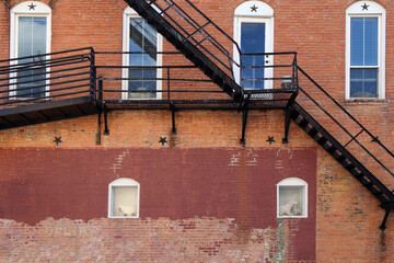 arched white windows behind back alley fire escape stairs at an old faded brick building