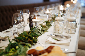 Decorative details on table made of flowers, green leaves and candles. Beautiful plates, glasses...