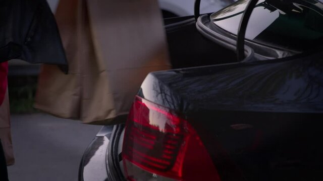 Beautiful Girl Is Putting Shopping Bags Into Car Trunk And Smiling. Loading Shopping Into Boot Of Car. Eco Paper Bags With Groceries From The Supermarket. Outdoor. Close-up.