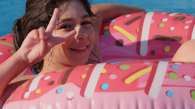 11-12 years old happy cute caucasian girl lying on an inflatable donut circle in the swimming pool in a garden. Cool summer holidays for children and kids. games on the water. Pink donat. 4k slow moti