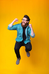 Fototapeta na wymiar Happy bearded hipster is jumping in a studio making winner gesture while screaming over yellow background.