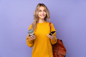 Teenager Russian student girl isolated on purple background holding coffee to take away and a mobile while thinking something