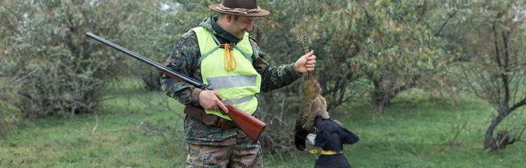 A man with a gun in his hands and an orange vest on a pheasant hunt in a wooded area in cloudy...