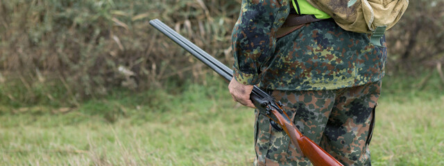 A man with a gun in his hands and an orange vest on a pheasant hunt in a wooded area in cloudy...