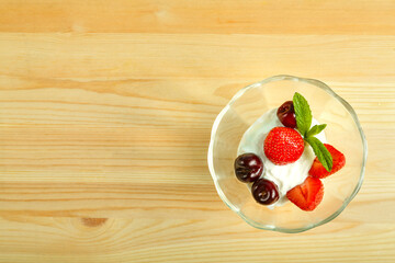 Ice cream dessert with strawberries and cherries in a bowl on a wooden table. Copy space.