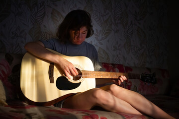 girl plays the guitar at home. Warm evening sunlight and yellow tones. self-development at home - 359775224