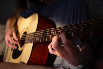 Close up photo of a girl plays the guitar at home. Warm evening sunlight and yellow tones. self-development at home - 359775299