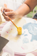 woman's hand painting pictures with paints on a day table