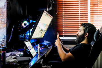bearded man gamer designer freelancer working on high end computer using smartphone
