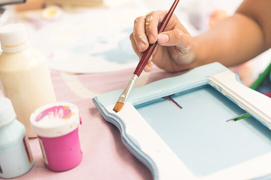 woman's hand painting pictures with paints on a day table