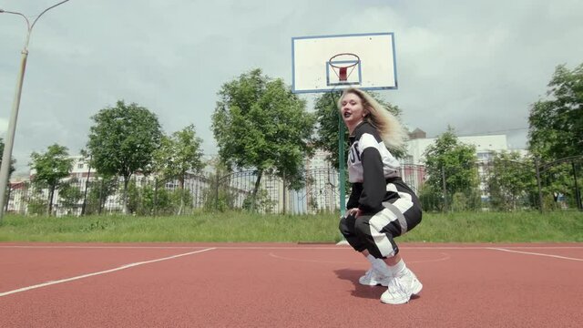 young woman with long hair in tracksuit dancing street modern dance, dancehall twerk on a Sportsground. Urban dancing freestyle in the city. Slow motion. Gimbal shot