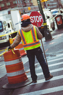 construction worker with stop sign orange traffic cone on busy city street